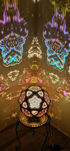 A colorful geometric patterned lamp casts shadows on a wall, with intricate designs created by the interplay of light and shadow.