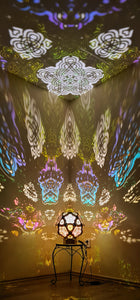 A colorful geometric patterned lamp casts shadows on a wall, with intricate designs created by the interplay of light and shadow.