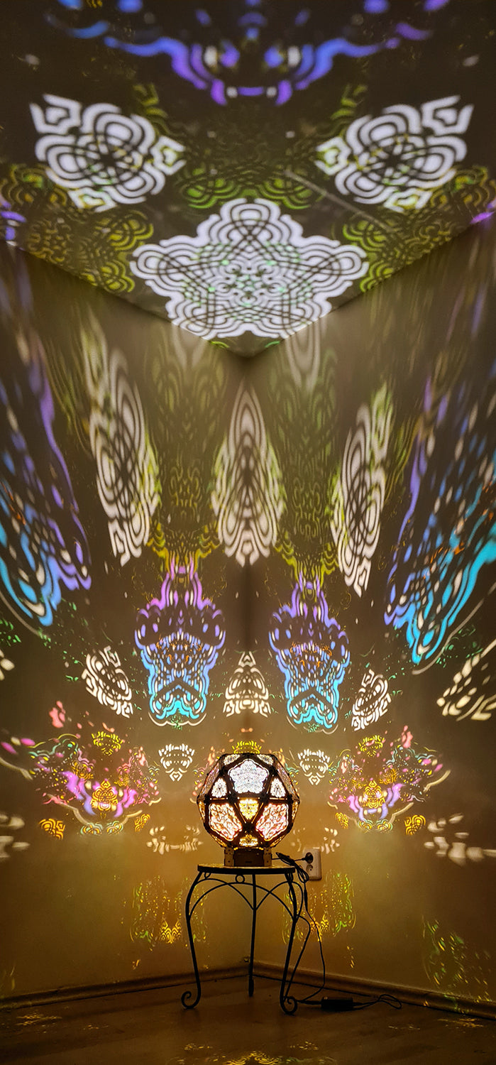 A colorful geometric patterned lamp casts shadows on a wall, with intricate designs created by the interplay of light and shadow.