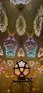 A colorful geometric patterned lamp casts shadows on a wall, with intricate designs created by the interplay of light and shadow.