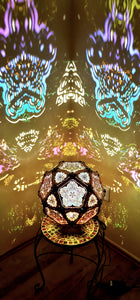 A colorful geometric patterned lamp casts shadows on a wall, with intricate designs created by the interplay of light and shadow.