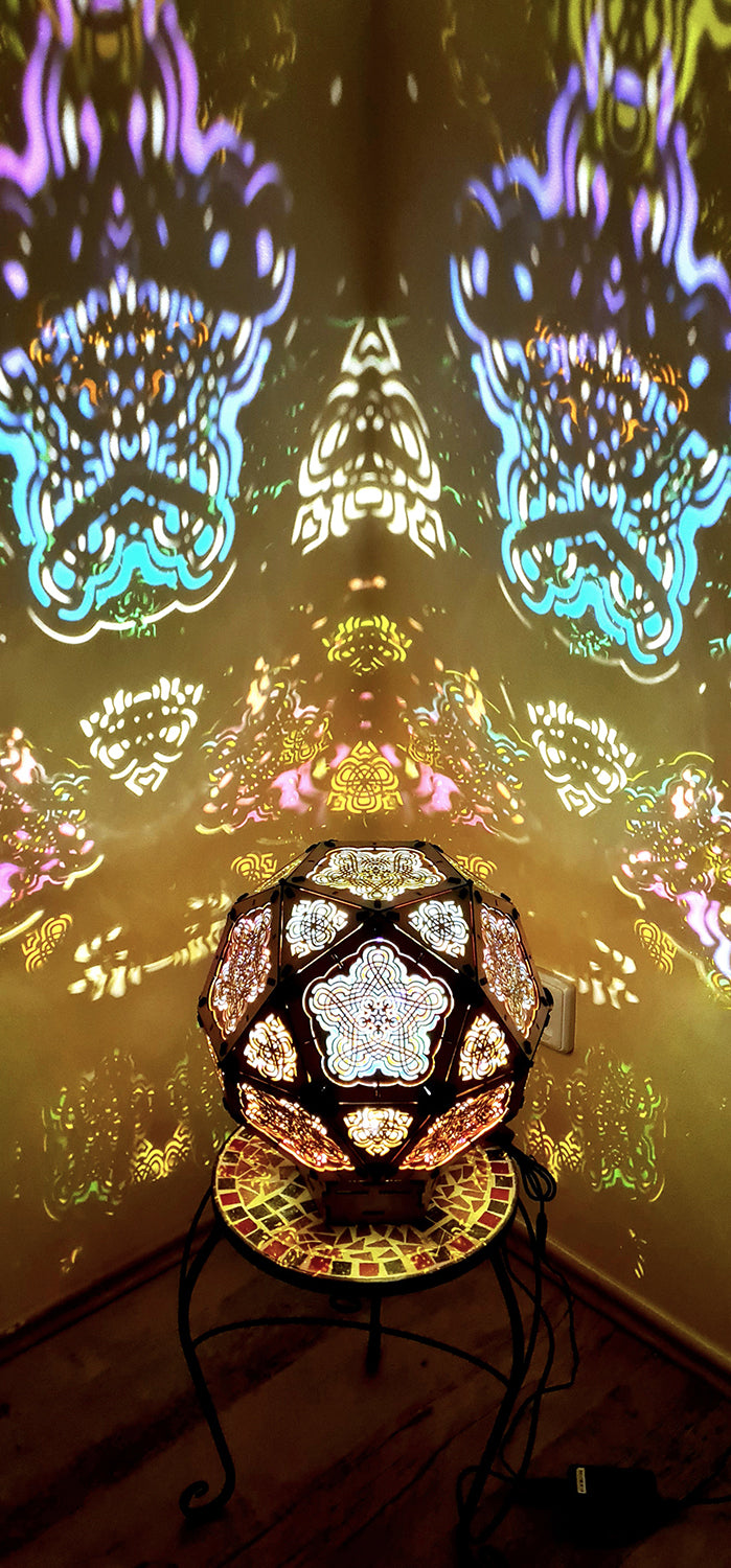 A colorful geometric patterned lamp casts shadows on a wall, with intricate designs created by the interplay of light and shadow.