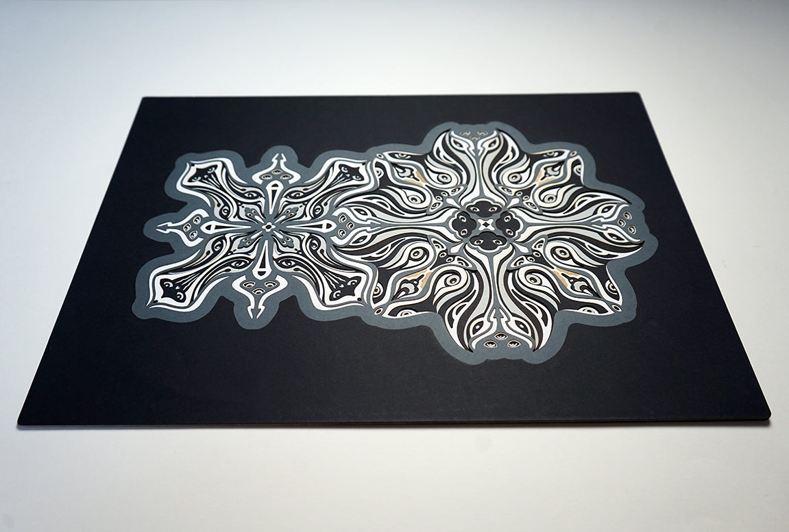 Monochrome layered paper artwork titled Metamorphs, made of intricate geometric mandalas that reveal totemic faces.
