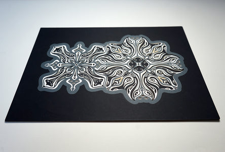 Monochrome layered paper artwork titled Metamorphs, made of intricate geometric mandalas that reveal totemic faces.