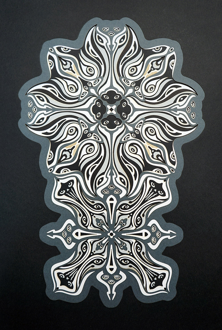 Monochrome layered paper artwork titled Metamorphs, made of intricate geometric mandalas that reveal totemic faces.