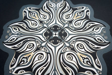 Monochrome layered paper artwork titled Metamorphs, made of intricate geometric mandalas that reveal totemic faces.