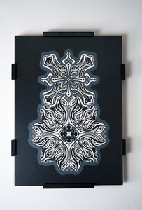 Monochrome layered paper artwork titled Metamorphs, made of intricate geometric mandalas that reveal totemic faces.