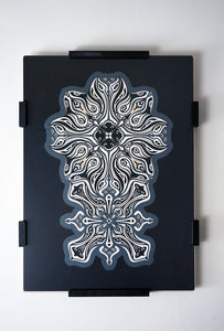 Monochrome layered paper artwork titled Metamorphs, made of intricate geometric mandalas that reveal totemic faces.