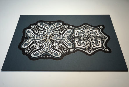 Monochrome layered paper artwork titled Metamorphs, made of intricate geometric mandalas that reveal totemic faces.