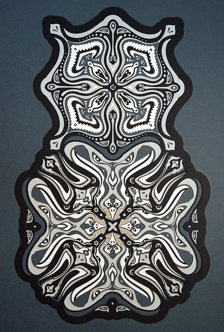 Monochrome layered paper artwork titled Metamorphs, made of intricate geometric mandalas that reveal totemic faces.