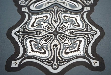 Monochrome layered paper artwork titled Metamorphs, made of intricate geometric mandalas that reveal totemic faces.