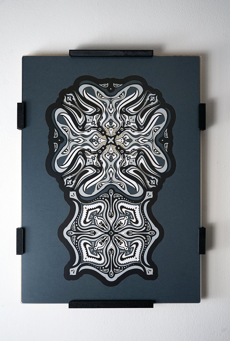 Monochrome layered paper artwork titled Metamorphs, made of intricate geometric mandalas that reveal totemic faces.