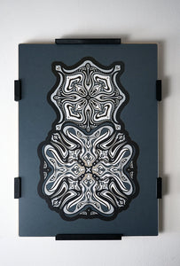 Monochrome layered paper artwork titled Metamorphs, made of intricate geometric mandalas that reveal totemic faces.