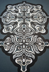 Monochrome layered paper artwork from the Metamorphs series, featuring interlocking mandalas that form hidden animal and spirit faces.