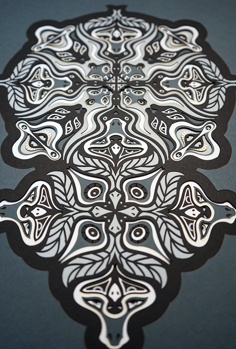 Monochrome layered paper artwork from the Metamorphs series, featuring interlocking mandalas that form hidden animal and spirit faces.