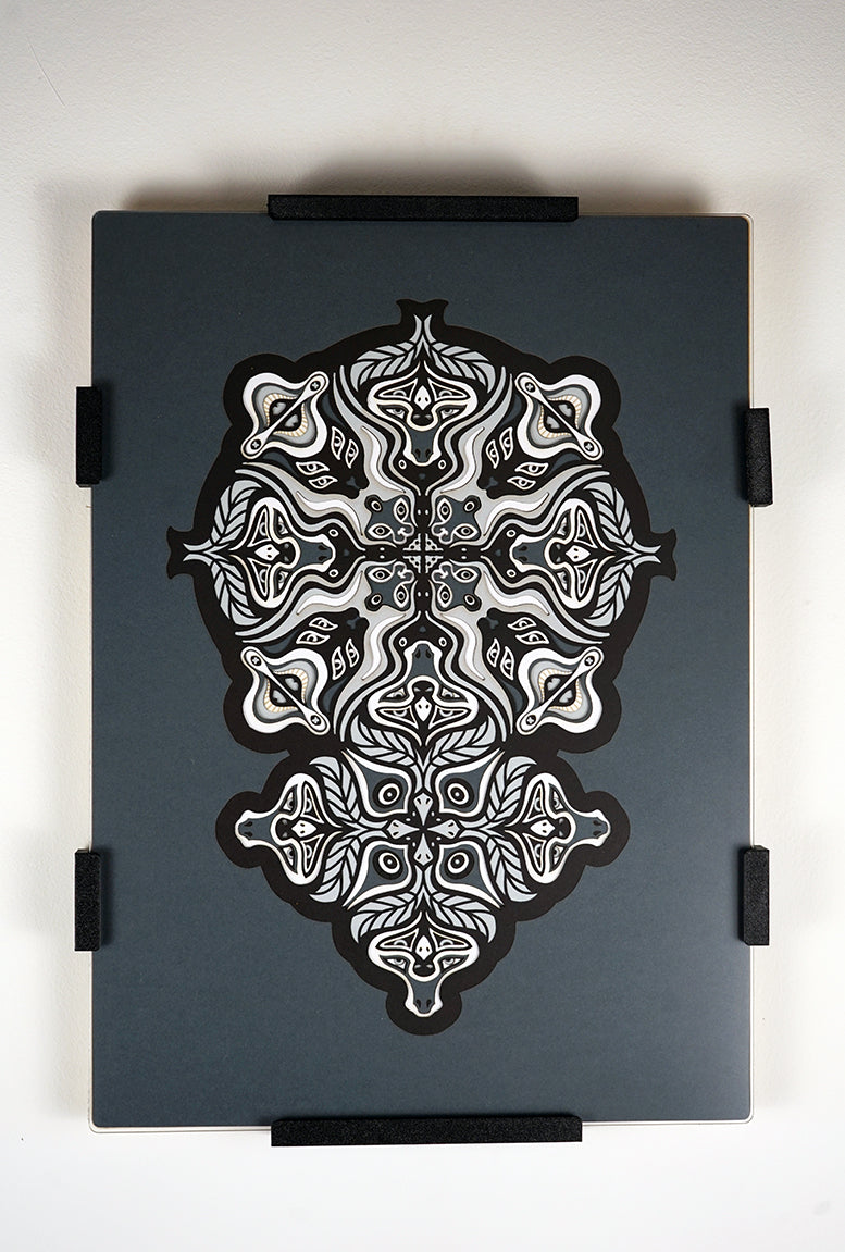 Monochrome layered paper artwork from the Metamorphs series, featuring interlocking mandalas that form hidden animal and spirit faces.