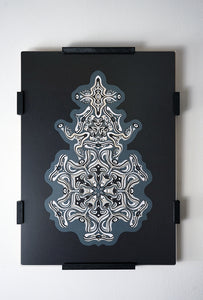 Intricate monochrome paper layers arranged in a mandala structure, creating emerging spirit faces and abstract creatures.