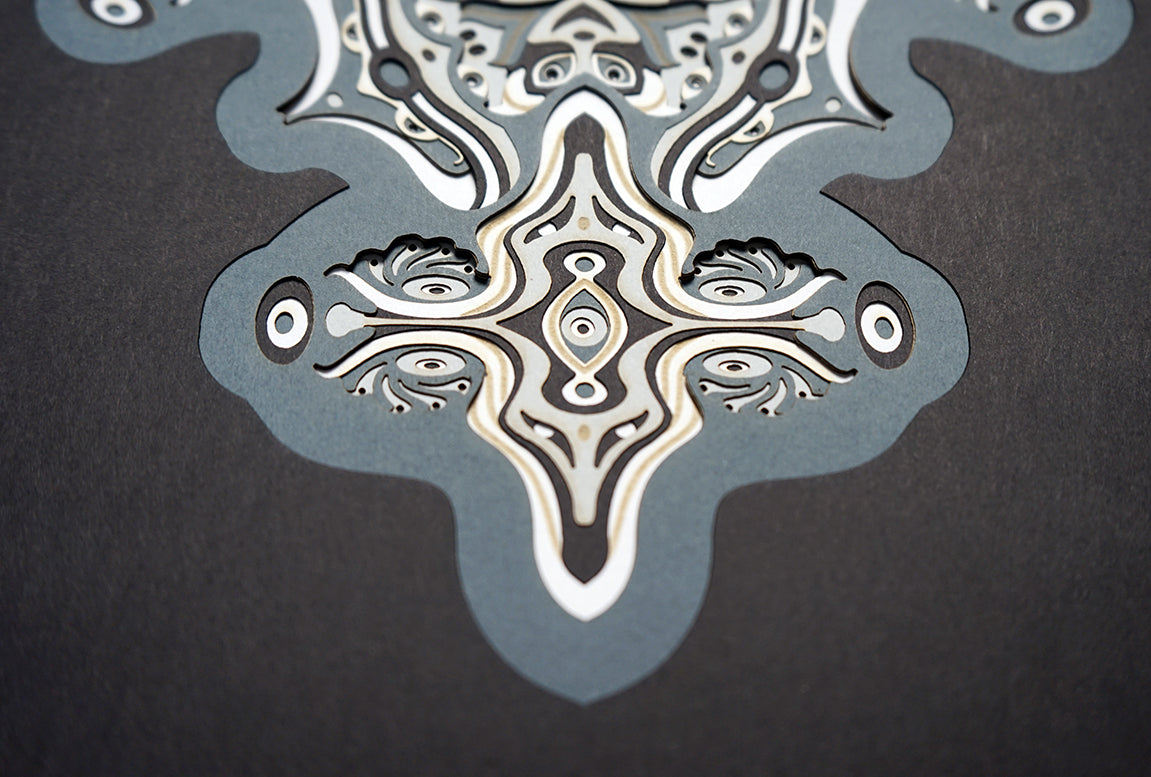 Intricate monochrome paper layers arranged in a mandala structure, creating emerging spirit faces and abstract creatures.