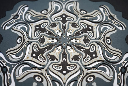 Intricate monochrome paper layers arranged in a mandala structure, creating emerging spirit faces and abstract creatures.