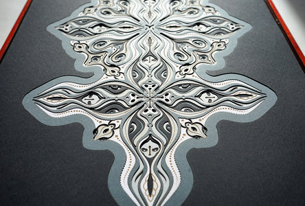 Layered grayscale paper forming symmetrical mandala patterns that reveal subtle, mask-like faces from the Metamorphs series