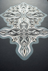 Layered grayscale paper forming symmetrical mandala patterns that reveal subtle, mask-like faces from the Metamorphs series