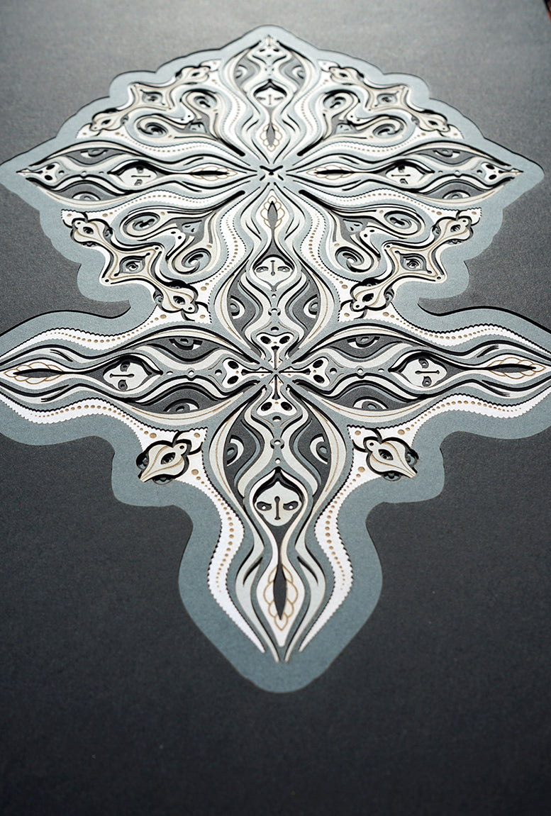 Layered grayscale paper forming symmetrical mandala patterns that reveal subtle, mask-like faces from the Metamorphs series