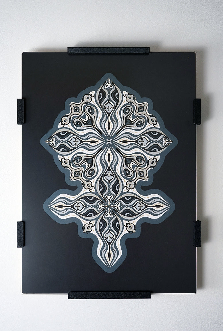 Layered grayscale paper forming symmetrical mandala patterns that reveal subtle, mask-like faces from the Metamorphs series