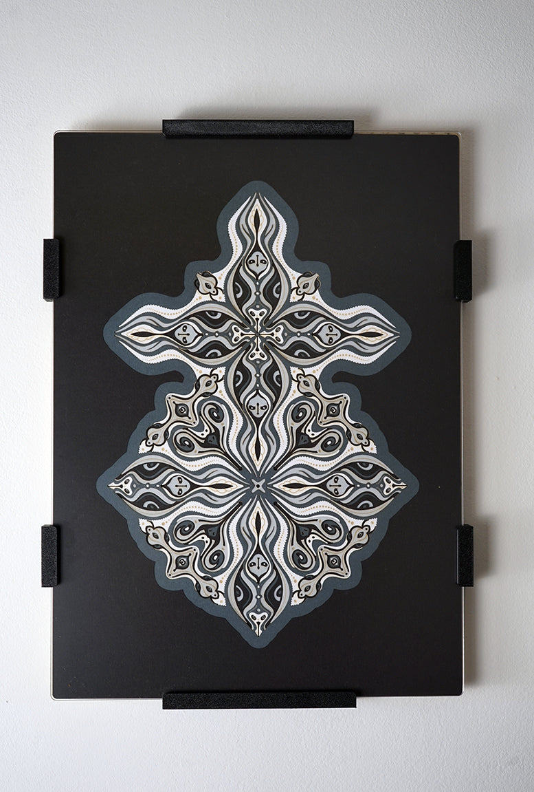 Layered grayscale paper forming symmetrical mandala patterns that reveal subtle, mask-like faces from the Metamorphs series