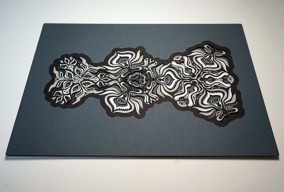 Black and white layered paper mandala with emerging animal spirit faces, part of the Metamorphs collection.