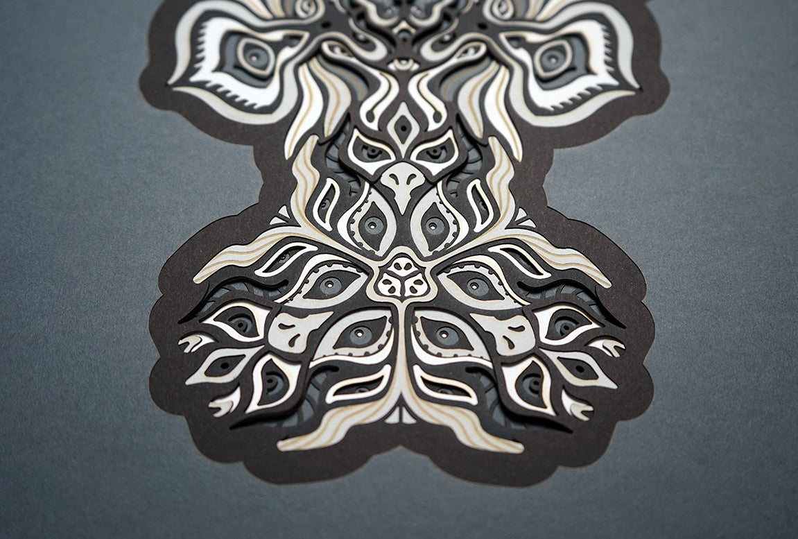 Black and white layered paper mandala with emerging animal spirit faces, part of the Metamorphs collection.