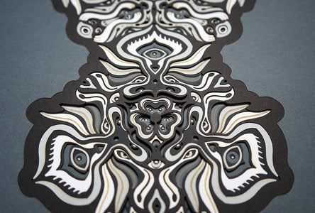Black and white layered paper mandala with emerging animal spirit faces, part of the Metamorphs collection.