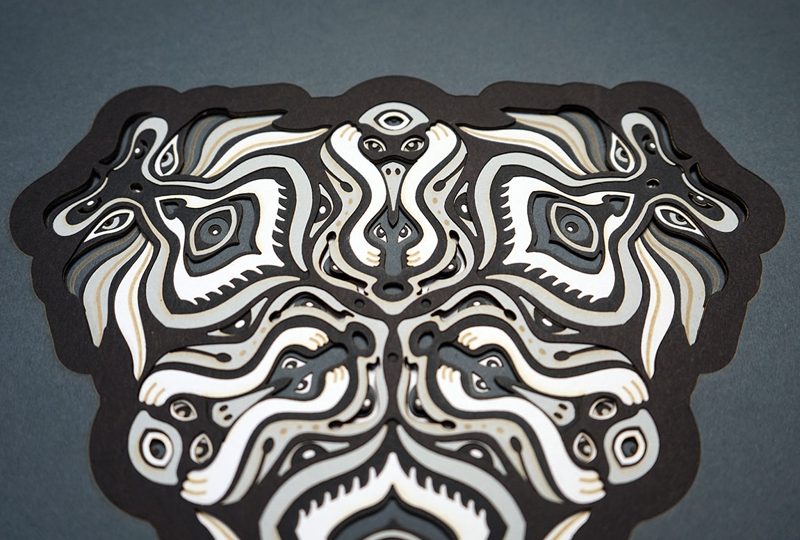 Black and white layered paper mandala with emerging animal spirit faces, part of the Metamorphs collection.