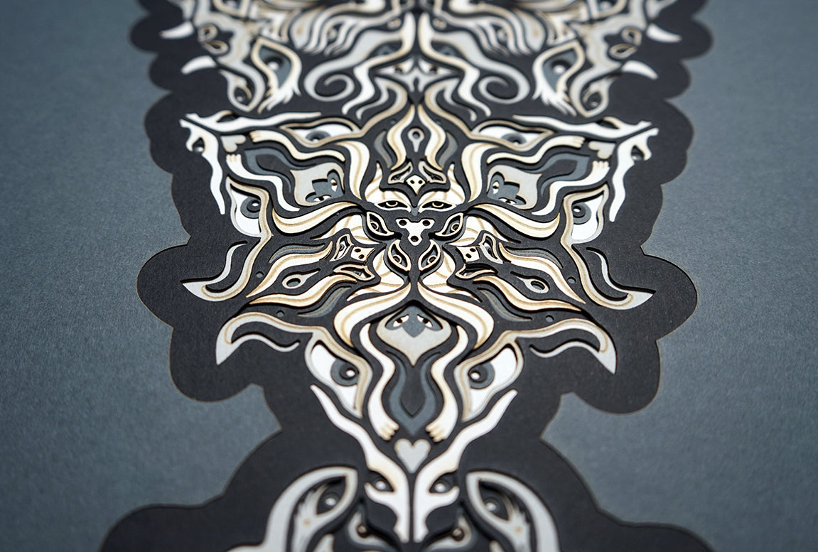 Geometric mandala made of layered grayscale paper, revealing masked spirit figures within the patterns.