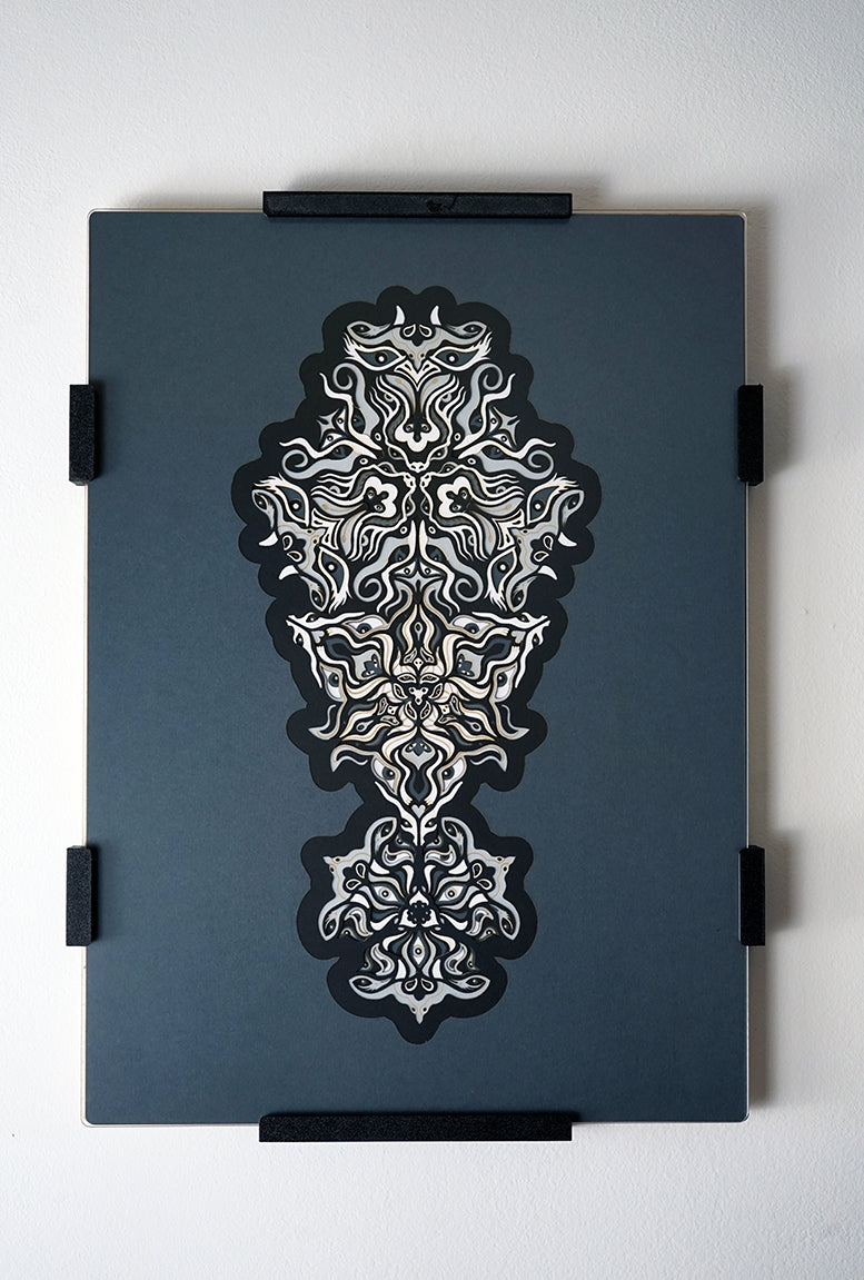 Geometric mandala made of layered grayscale paper, revealing masked spirit figures within the patterns.