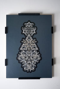 Geometric mandala made of layered grayscale paper, revealing masked spirit figures within the patterns.