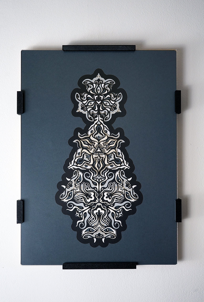 Geometric mandala made of layered grayscale paper, revealing masked spirit figures within the patterns.