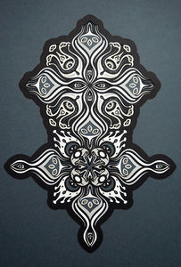Intricate paper cut mandala in shades of black and white, with morphing faces appearing between the layers.