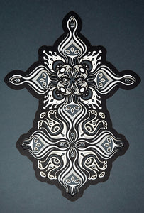 Intricate paper cut mandala in shades of black and white, with morphing faces appearing between the layers.