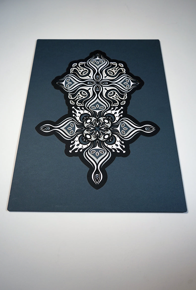 Intricate paper cut mandala in shades of black and white, with morphing faces appearing between the layers.