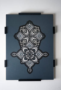 Intricate paper cut mandala in shades of black and white, with morphing faces appearing between the layers.