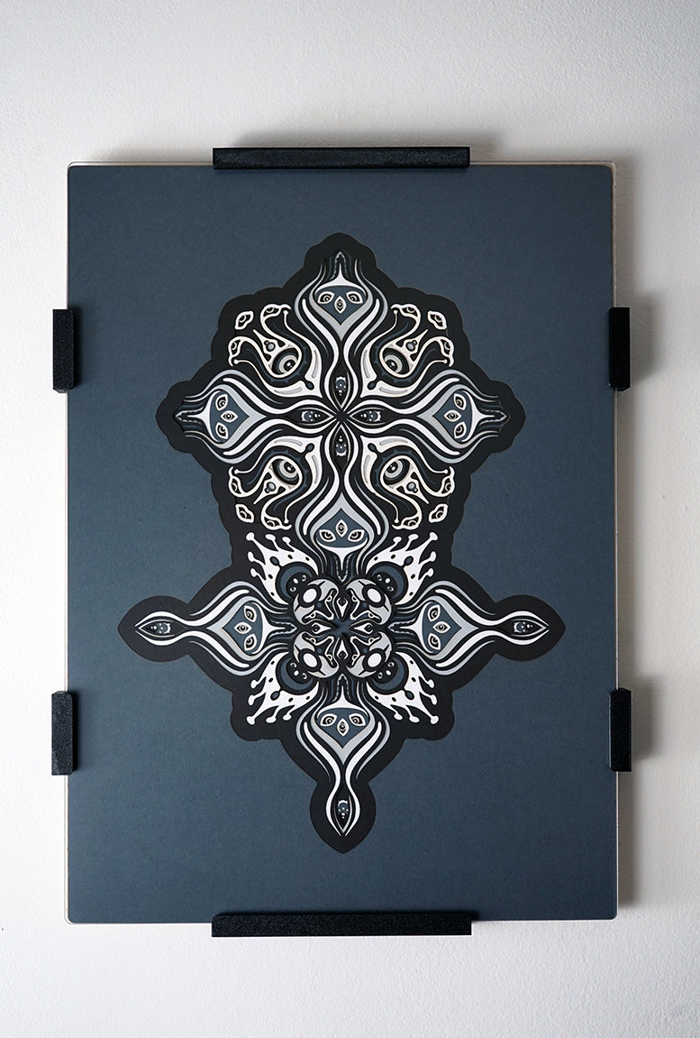 Intricate paper cut mandala in shades of black and white, with morphing faces appearing between the layers.