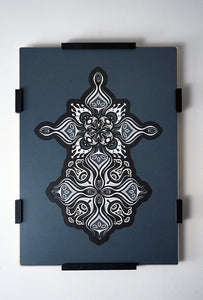 Intricate paper cut mandala in shades of black and white, with morphing faces appearing between the layers.