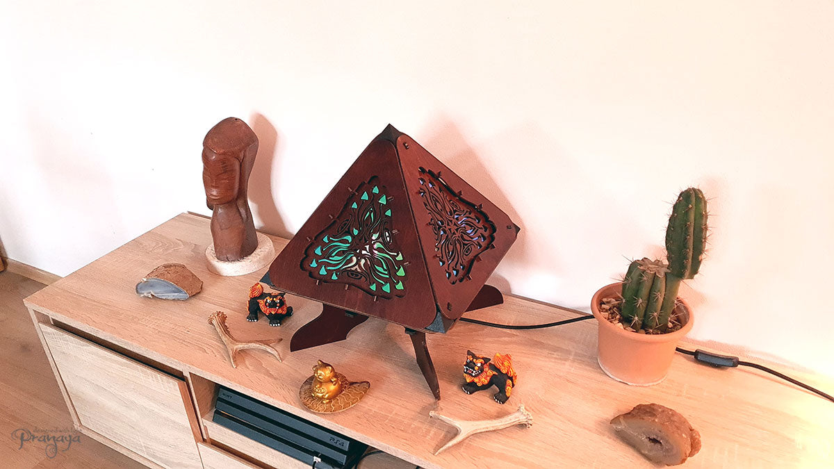 A colorful shadow lamp with a geometric design, featuring triangular sides and a pyramid shape, projecting a vibrant mushroom pattern on a wall.