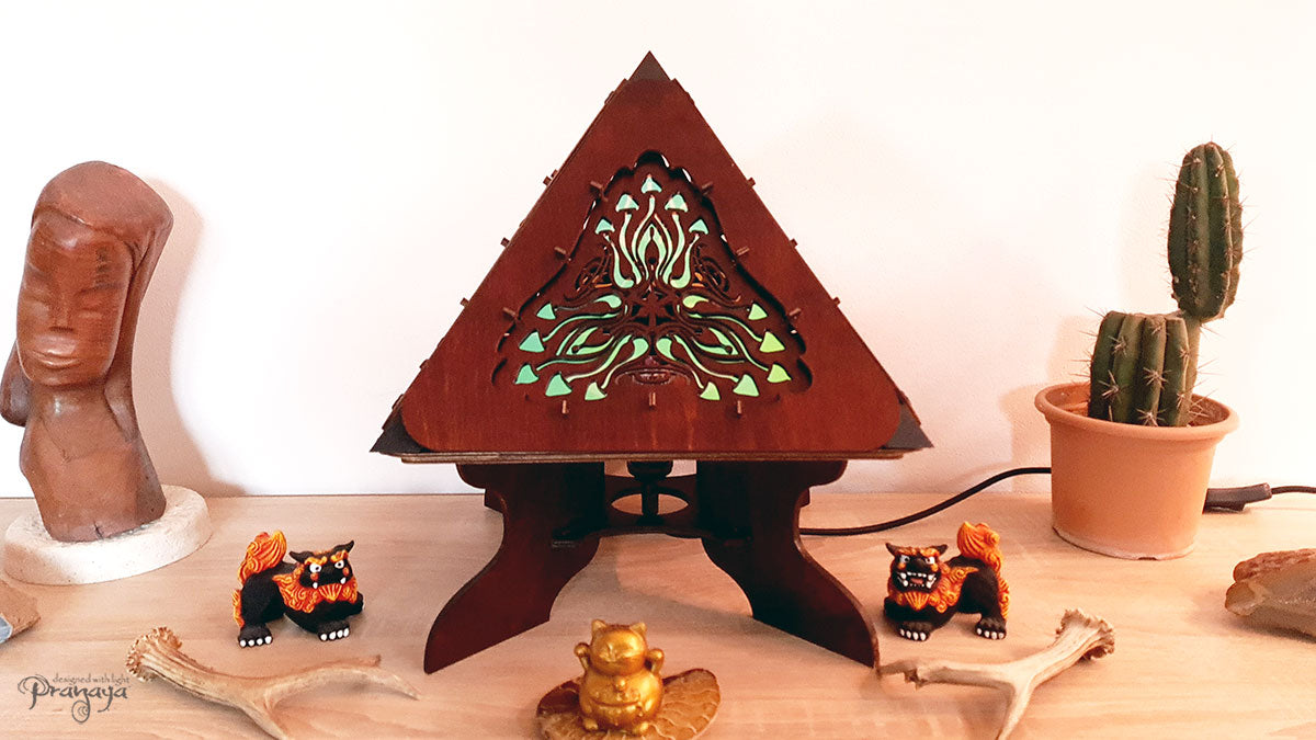 A colorful shadow lamp with a geometric design, featuring triangular sides and a pyramid shape, projecting a vibrant mushroom pattern on a wall.