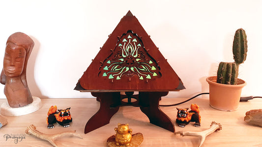 A colorful shadow lamp with a geometric design, featuring triangular sides and a pyramid shape, projecting a vibrant mushroom pattern on a wall.
