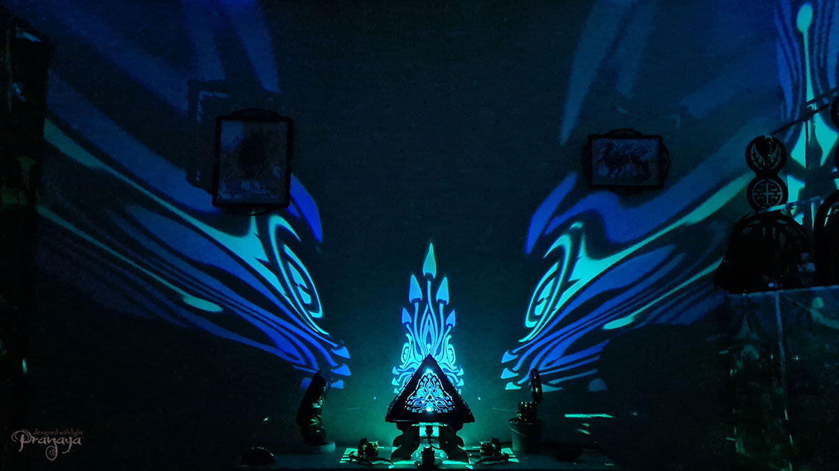 A colorful shadow lamp with a geometric design, featuring triangular sides and a pyramid shape, projecting a vibrant mushroom pattern on a wall.