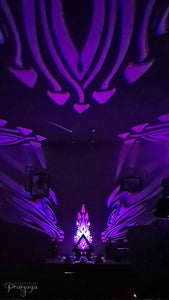 A colorful shadow lamp with a geometric design, featuring triangular sides and a pyramid shape, projecting a vibrant mushroom pattern on a wall.