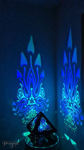 A colorful shadow lamp with a geometric design, featuring triangular sides and a pyramid shape, projecting a vibrant mushroom pattern on a wall.