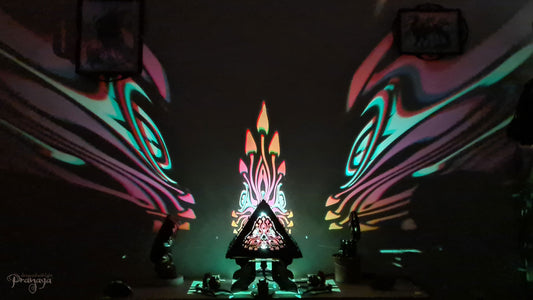 A colorful shadow lamp with a geometric design, featuring triangular sides and a pyramid shape, projecting a vibrant mushroom pattern on a wall.