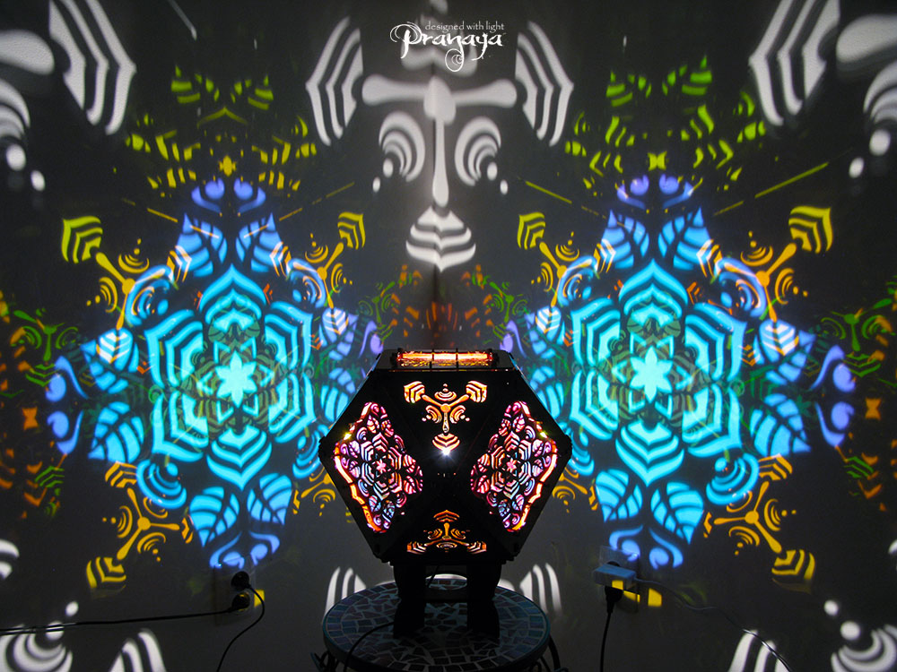 A colorful kaleidoscopic shadow lamp with a geometric pattern, showcasing a cuboctahedron shape with intricate cut-outs, mounted on a stand.